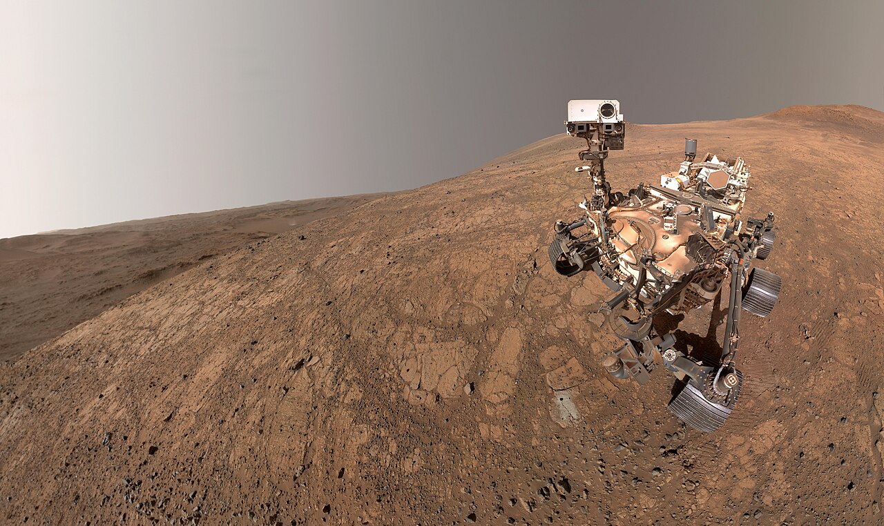 A Perseverance marsjáró 2025-ben készült önarcképe a Marson, a háttérben egy távoli porördöggel. NASA/JPL-Caltech/MSSS.