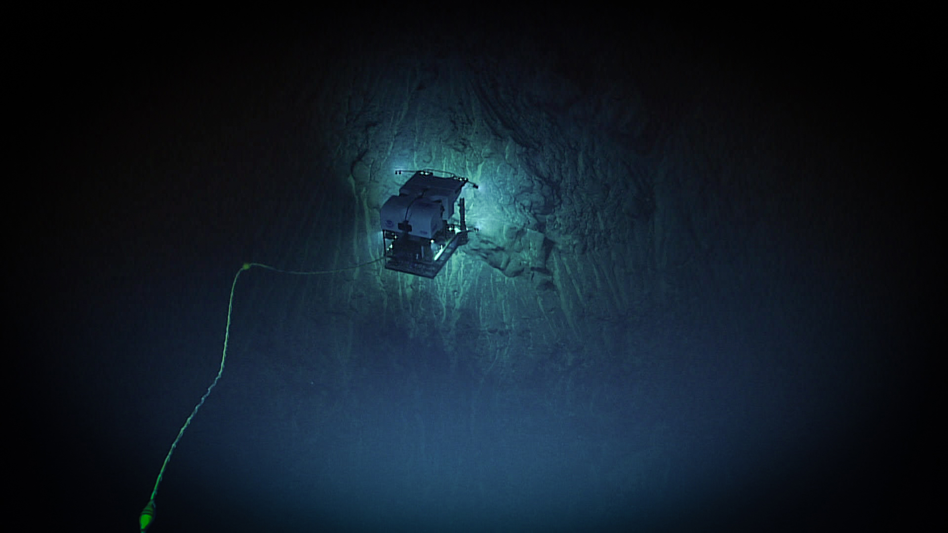A NOAA Deep Discoverer mélytengeri robotja a Murray-törészóna megvilágított sziklafala előtt, 4755 méter mélyen. NOAA Ocean Exploration, 2025 Beyond the Blue.